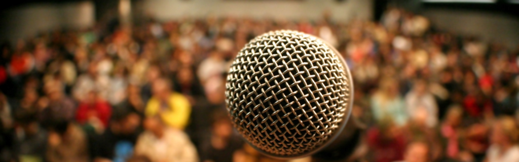 A person standing on a podium with a microphone, surrounded by a crowd of people. The person is giving a speech, with the audience engaged and listening attentively. The message is clear that establishing yourself as an authority in your niche is essential for scaling your business to seven figures.

